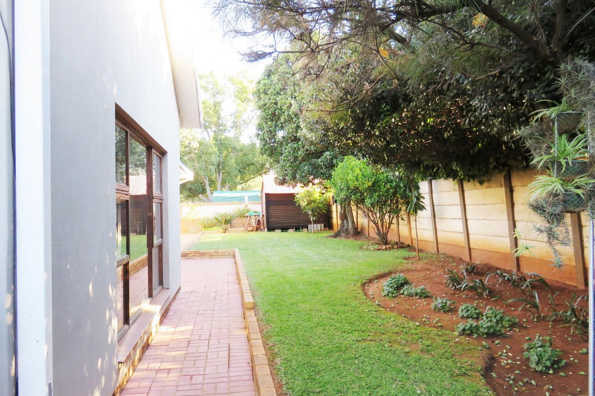 A private rear garden featuring a paved walkway, established trees, landscaped garden beds, and a secure precast concrete boundary wall.