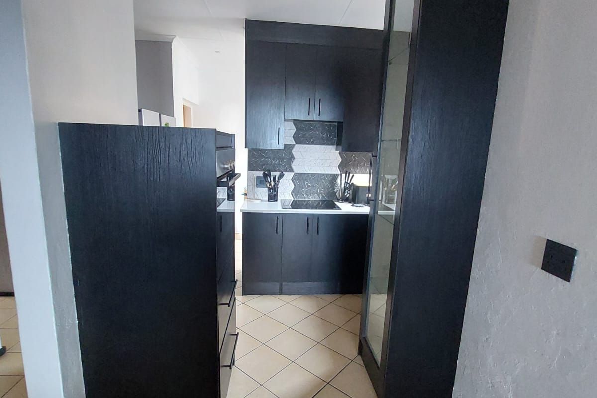 A compact kitchen featuring dark built-in cabinetry, a built-in oven, a hob, and a tiled backsplash with neutral floor tiles.