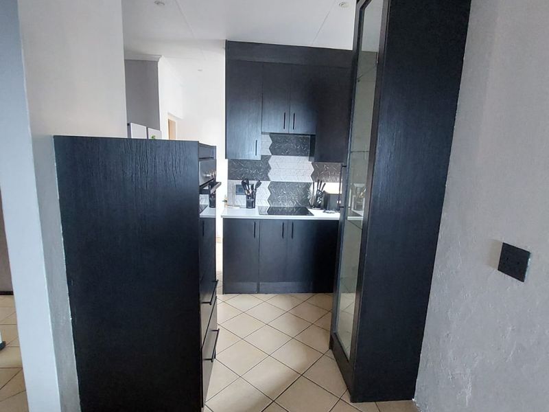 A compact kitchen featuring dark built-in cabinetry, a built-in oven, a hob, and a tiled backsplash with neutral floor tiles.