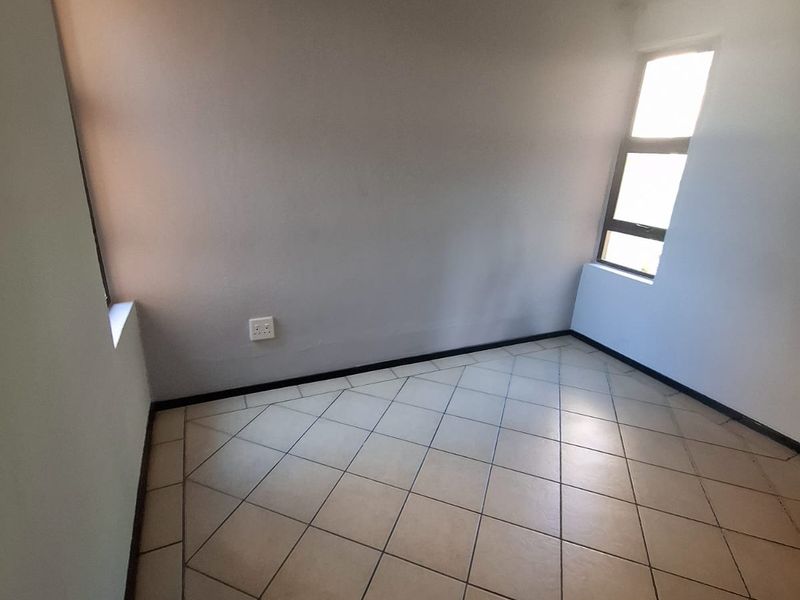 An empty bedroom featuring neutral tiled flooring and natural light from aluminium-framed windows, ready for personalization.