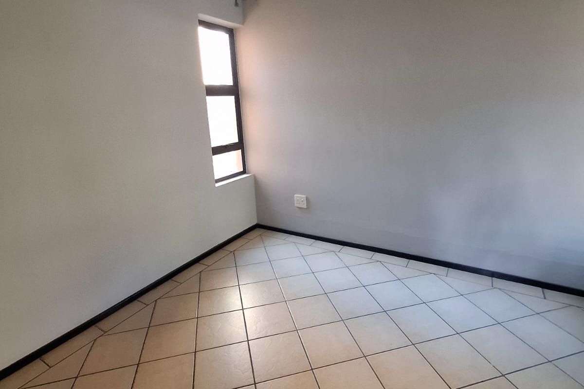 A clean, empty bedroom featuring neutral wall paint, tiled flooring, and a single window with a fitted curtain rod.