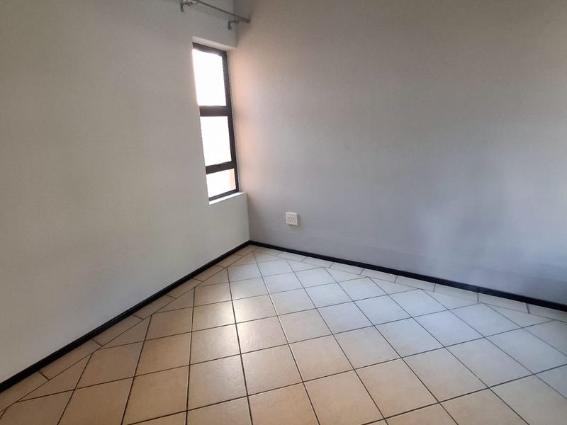 A clean, empty bedroom featuring neutral wall paint, tiled flooring, and a single window with a fitted curtain rod.