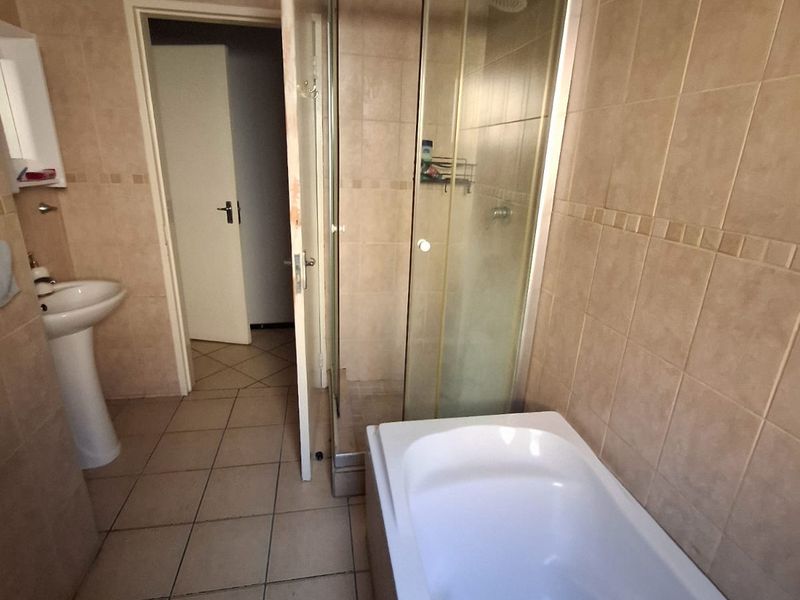 A functional bathroom featuring a pedestal basin, a separate shower enclosure, and a bathtub, finished with neutral ceramic wall and floor tiles.