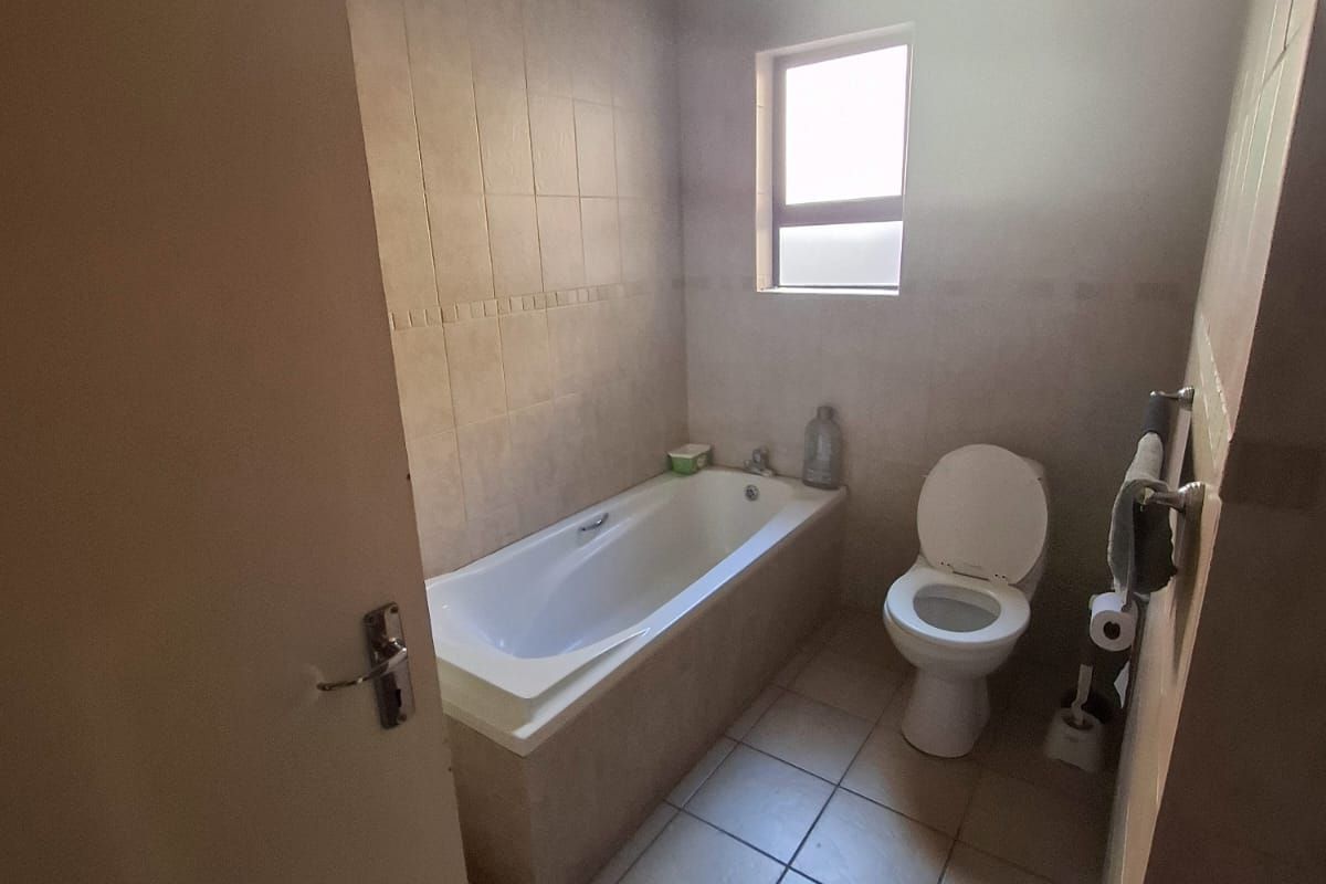 A functional bathroom featuring a built-in bathtub, toilet, and neutral tiled finishes throughout.