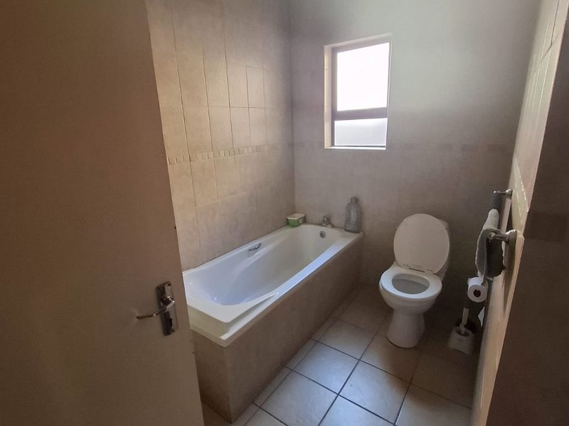 A functional bathroom featuring a built-in bathtub, toilet, and neutral tiled finishes throughout.