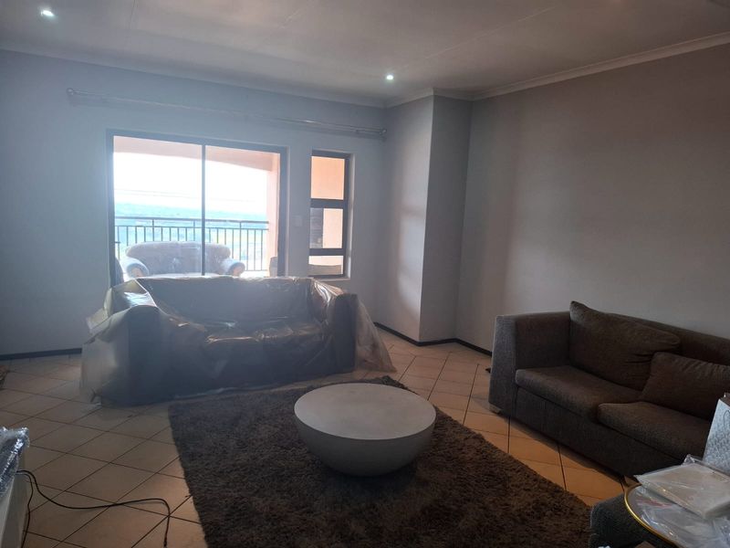 A spacious living room featuring tiled flooring, recessed lighting, and a sliding glass door providing access to an outdoor balcony area.