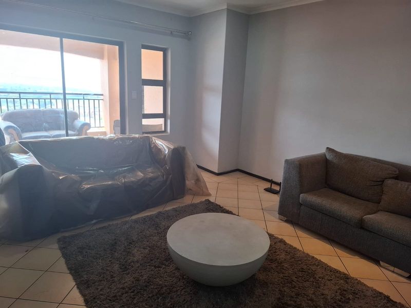 A living room featuring tiled flooring, neutral walls, and a sliding glass door providing access to an outdoor balcony area.