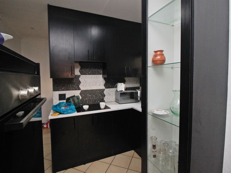 A compact kitchen featuring dark cabinetry, a modern geometric tiled backsplash, built-in oven and hob, and integrated glass display shelving.
