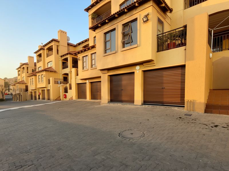 Exterior view of an apartment complex featuring multiple roller garage doors, balconies, and a paved driveway area.