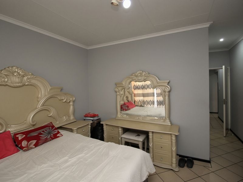 A bedroom featuring tiled flooring, neutral grey walls, and coved ceiling details, providing a functional and well-lit sleeping space.