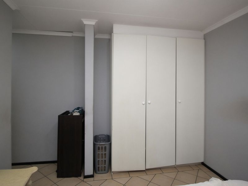 A bedroom featuring neutral grey walls, tiled flooring, and white built-in cupboards providing ample storage space.