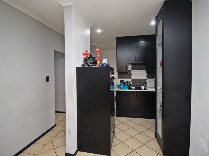 Compact kitchen featuring dark built-in cabinetry, tiled flooring, a hob with extractor fan, and a geometric tiled backsplash.
