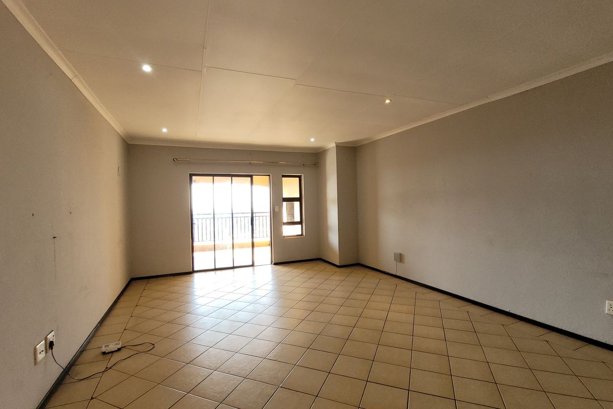 A spacious, empty living room featuring neutral tiled flooring, recessed downlighting, and a sliding glass door providing access to an outdoor area.