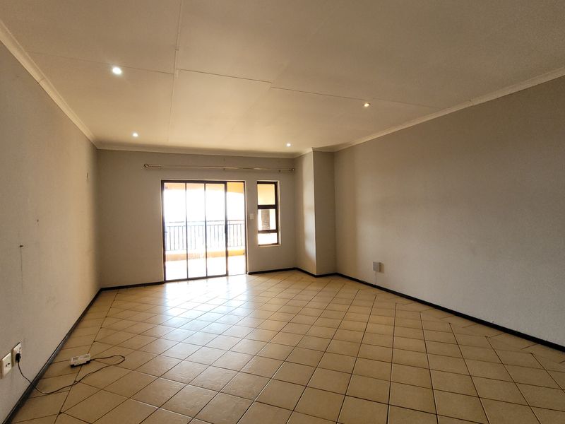 A spacious, empty living room featuring neutral tiled flooring, recessed downlighting, and a sliding glass door providing access to an outdoor area.
