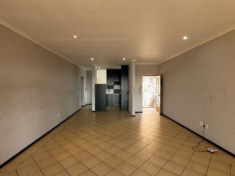 An open-plan living area featuring tiled flooring, recessed lighting, and a compact kitchen space, leading to an exterior entrance.