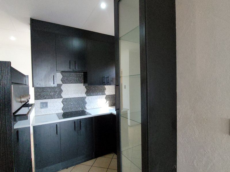 Modern kitchen featuring dark cabinetry, a sleek hob, extractor fan, and a stylish geometric tiled backsplash with integrated glass display shelving.