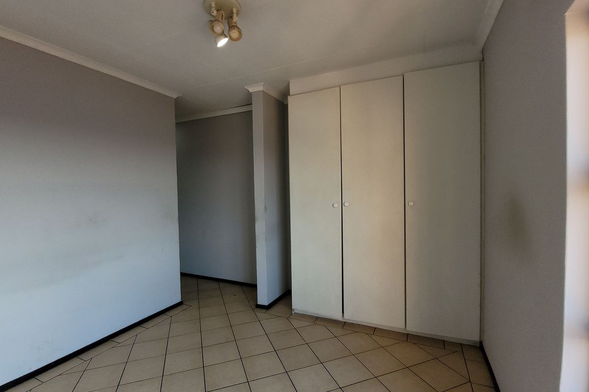 An empty bedroom featuring tiled flooring, built-in cupboards, and neutral wall finishes, offering a blank canvas for personalization.