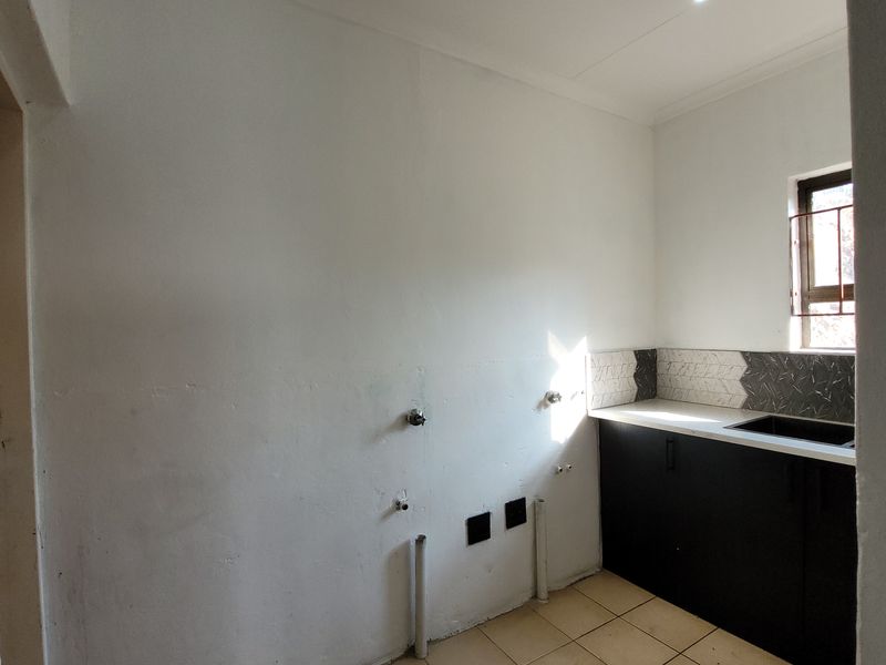 A functional laundry area featuring built-in cabinetry, a sink, tiled backsplash, and plumbing connections ready for appliance installation.