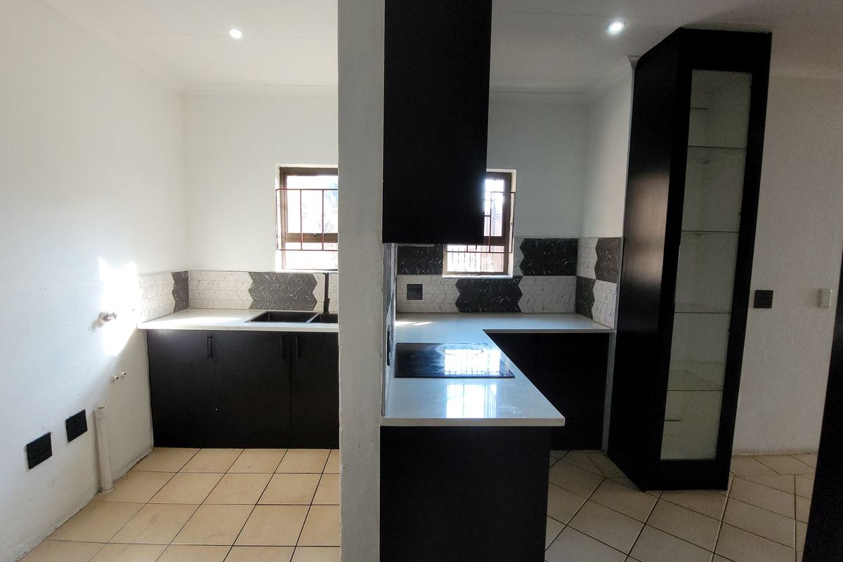 A modern kitchen featuring dark cabinetry, stone countertops, an electric hob, and tiled backsplash, currently vacant and awaiting final plumbing finishes.