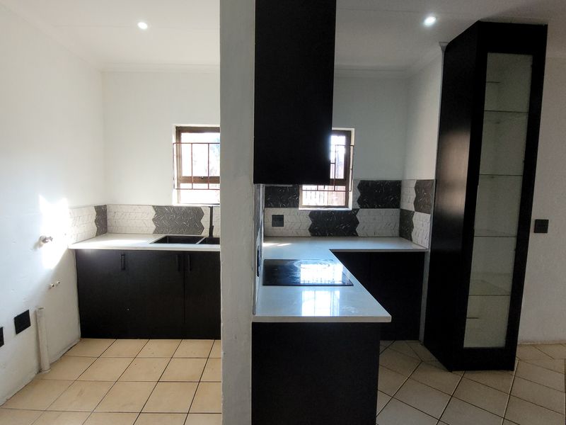 A modern kitchen featuring dark cabinetry, stone countertops, an electric hob, and tiled backsplash, currently vacant and awaiting final plumbing finishes.