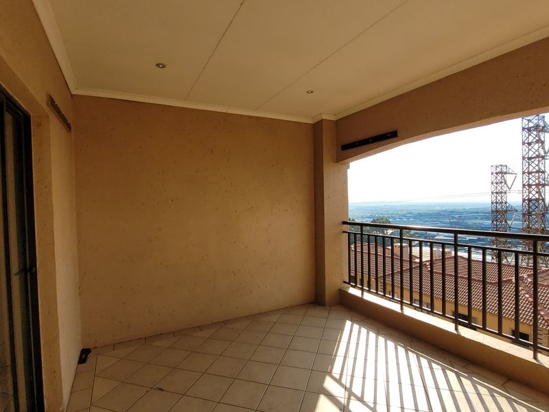 A spacious covered balcony featuring tiled flooring, a metal balustrade, and expansive elevated views of the surrounding area.
