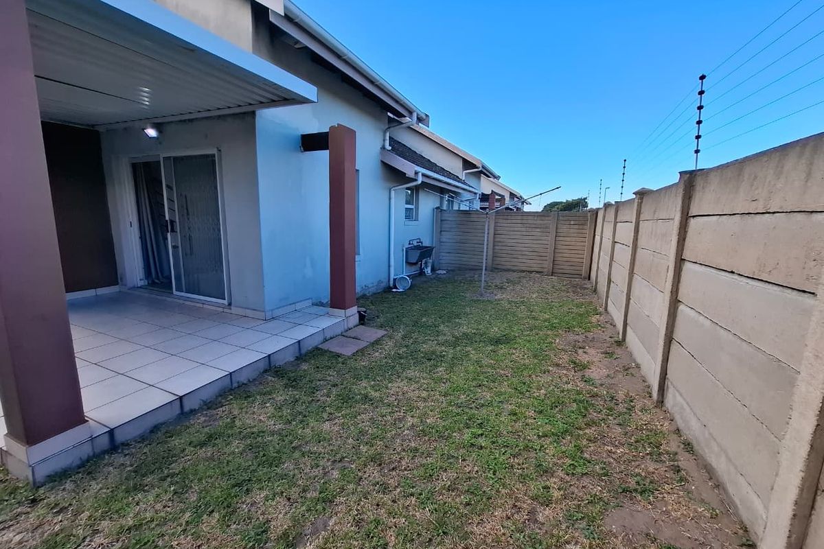 A private rear garden featuring a covered patio area, tiled flooring, and a perimeter boundary wall with electric fencing.