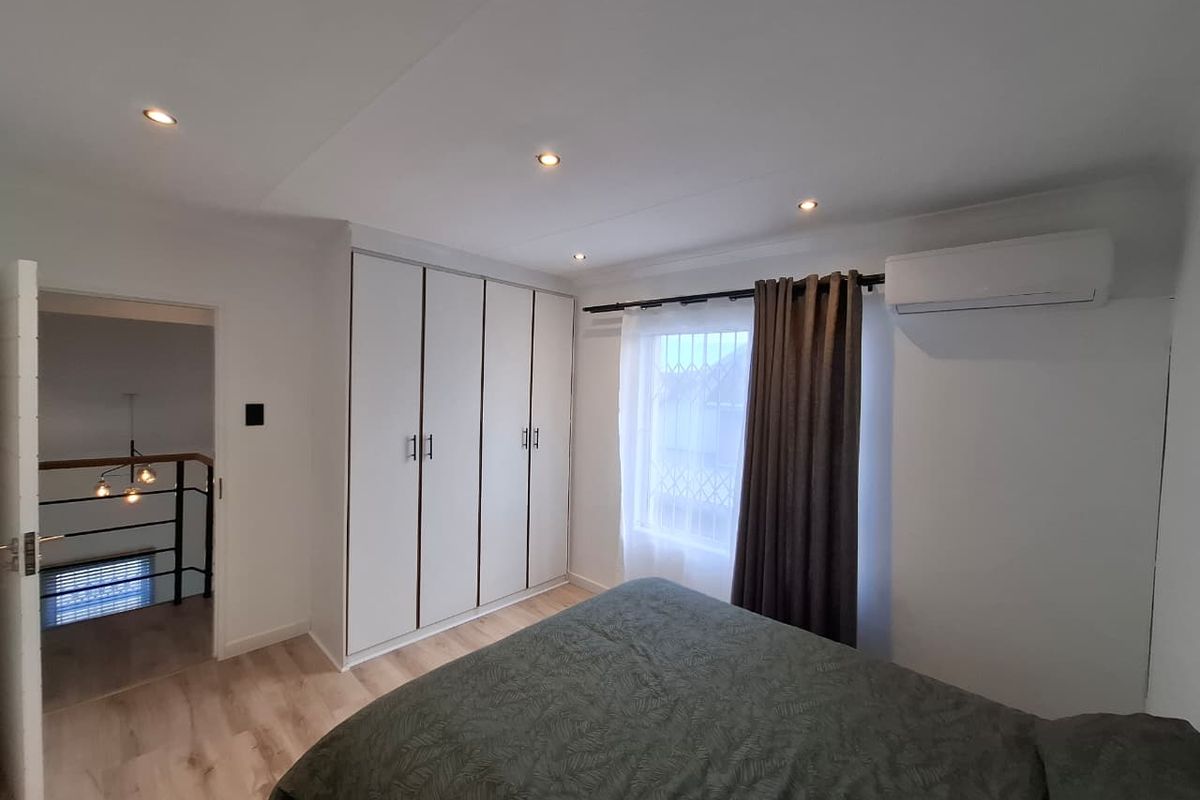 A well-maintained bedroom featuring built-in wardrobes, recessed ceiling lighting, light wood-look flooring, and a wall-mounted air conditioning unit.