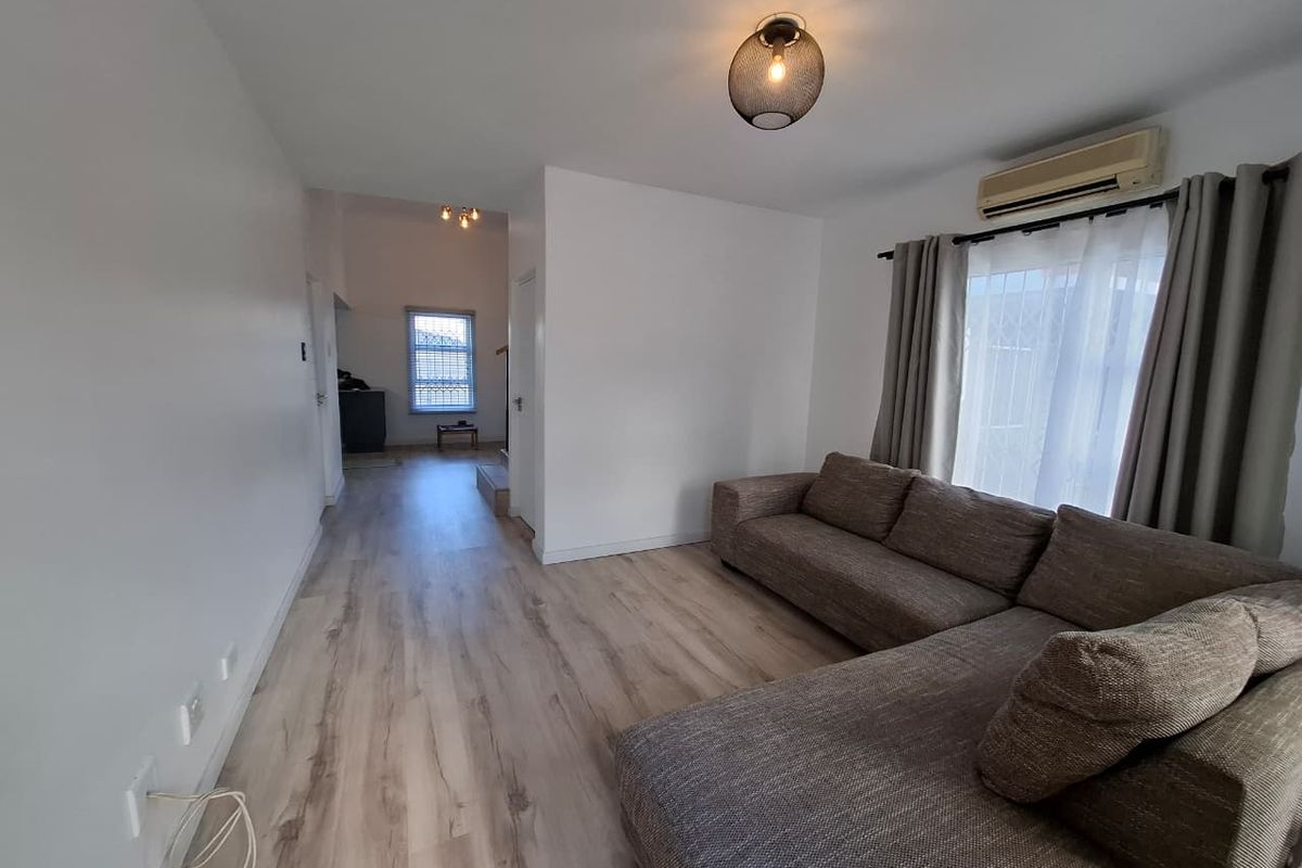 A bright living room featuring light wood-look laminate flooring, a wall-mounted air conditioning unit, and a modern pendant light fixture.
