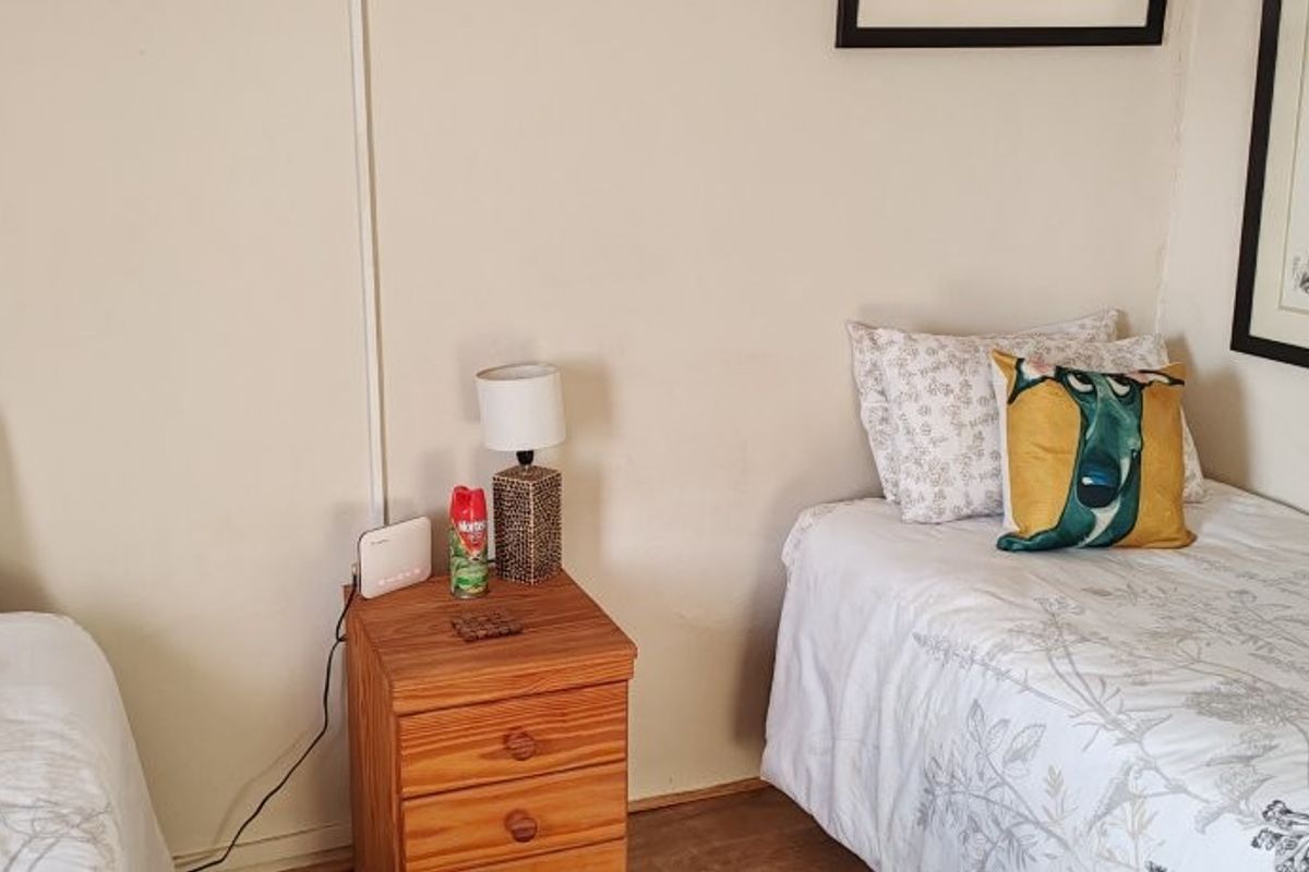 A bedroom featuring two single beds with neutral bedding and a central wooden bedside table.