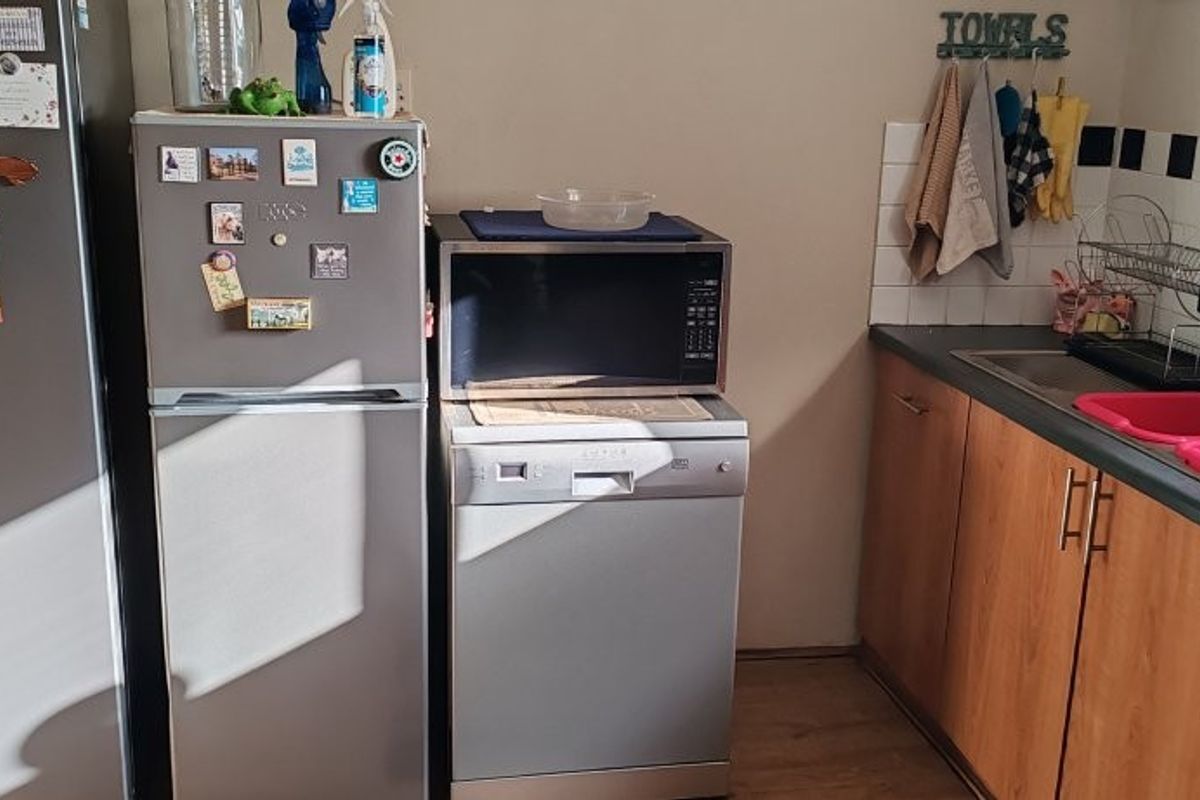 A functional kitchen area featuring wood-finish cabinetry, a stainless steel sink, and tiled splashback, providing essential prep and wash-up space.