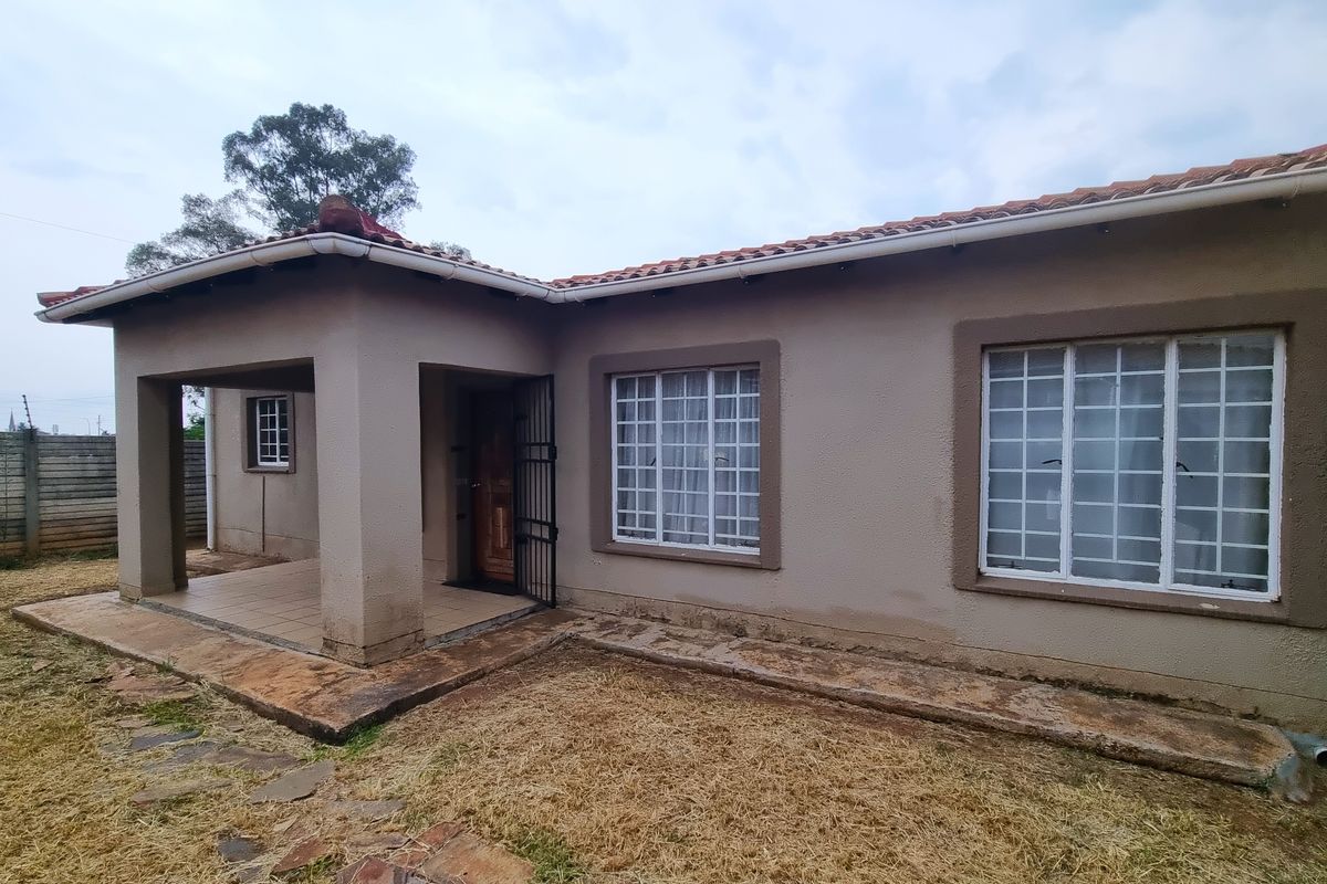 Rear view of the townhouse featuring a covered patio, tiled roof, and security bars on windows, set against a concrete boundary wall.