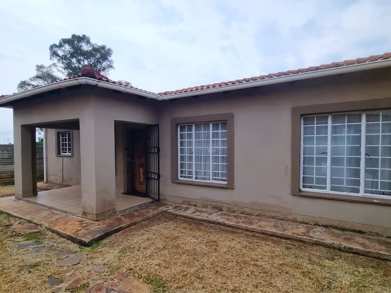 Rear view of the townhouse featuring a covered patio, tiled roof, and security bars on windows, set against a concrete boundary wall.