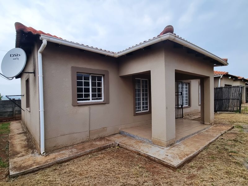 Rear view of the townhouse featuring a covered patio, tiled roof, and security bars on the windows.
