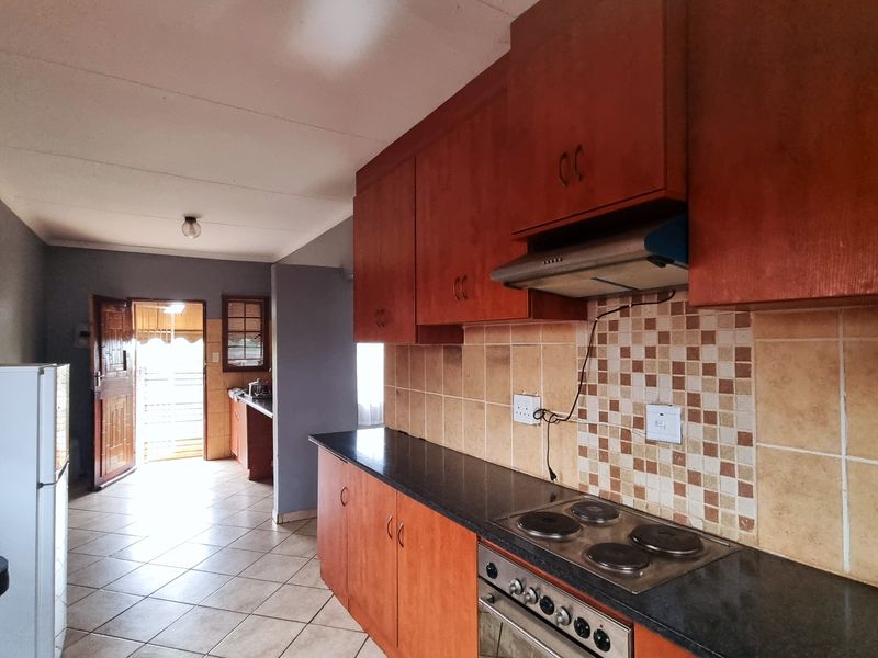 Functional kitchen featuring wooden cabinetry, built-in oven and hob, tiled backsplash, and direct access to the exterior entrance.
