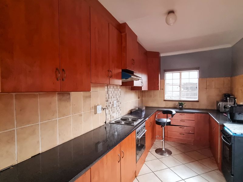 A functional kitchen featuring wooden cabinetry, granite countertops, a built-in oven with hob, and tiled flooring, offering a practical layout for daily meal preparation.