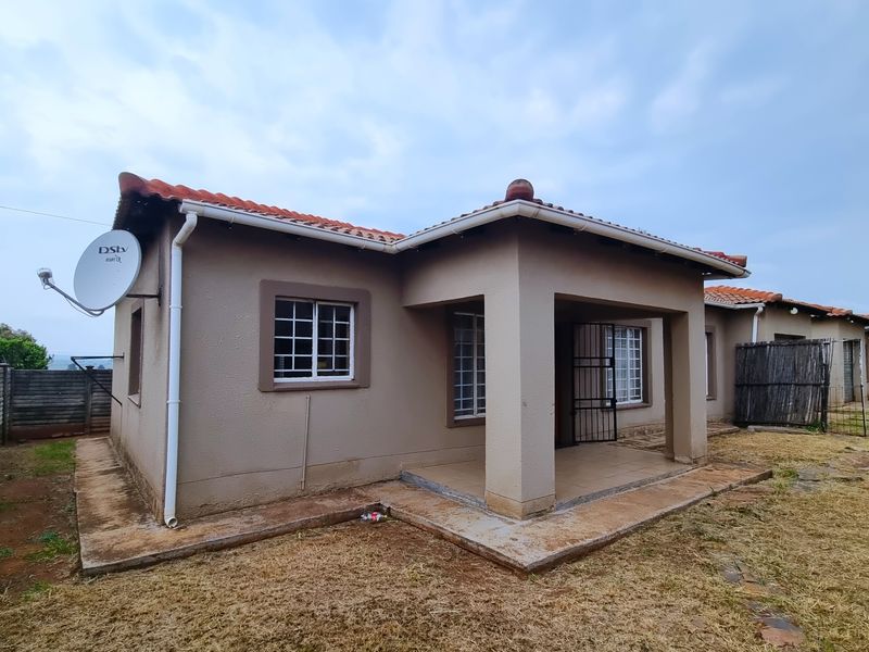 Rear view of the townhouse featuring a covered patio, tiled roof, and a private garden area with perimeter fencing.