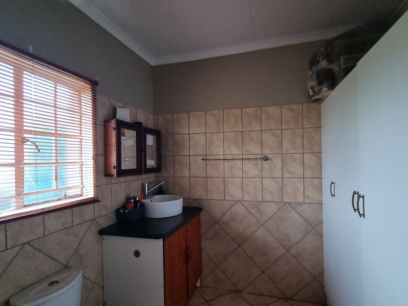 A functional bathroom featuring a vessel sink on a vanity cabinet, tiled walls and flooring, and built-in storage cupboards.