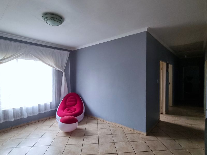 A spacious living area featuring neutral grey walls, tiled flooring, and natural light from a large window.