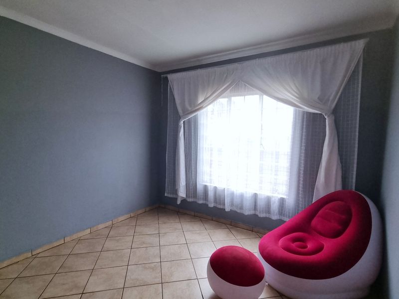 A neutrally painted bedroom featuring tiled flooring and a large window with installed curtain tracks, offering a blank canvas for personalization.