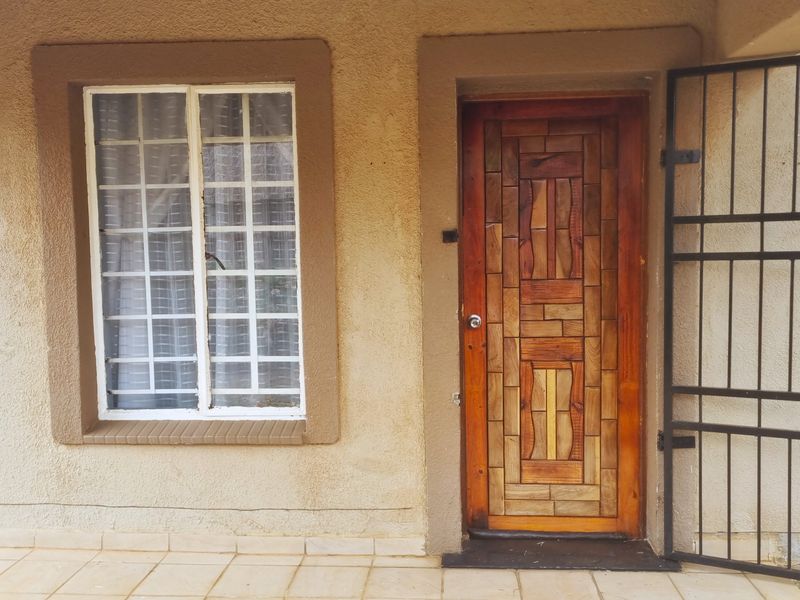 Front entrance featuring a decorative wooden door, security gate, and window with security bars, set on a tiled porch area.