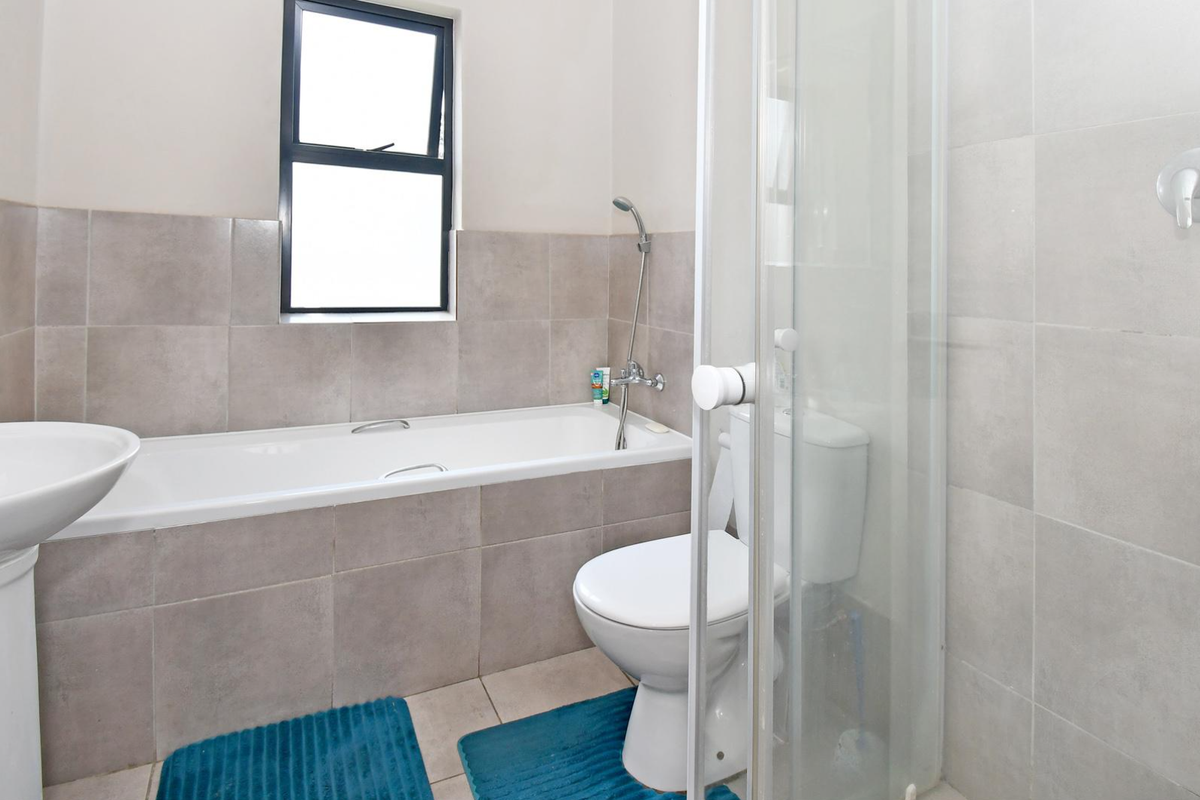 A functional bathroom featuring a pedestal basin, built-in bathtub, separate shower enclosure, and neutral ceramic tiling throughout.