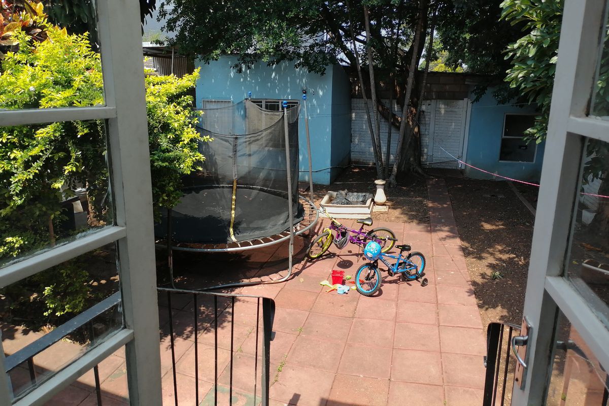 A view of the rear garden area featuring paved flooring, mature trees, and direct access from the interior through double doors.