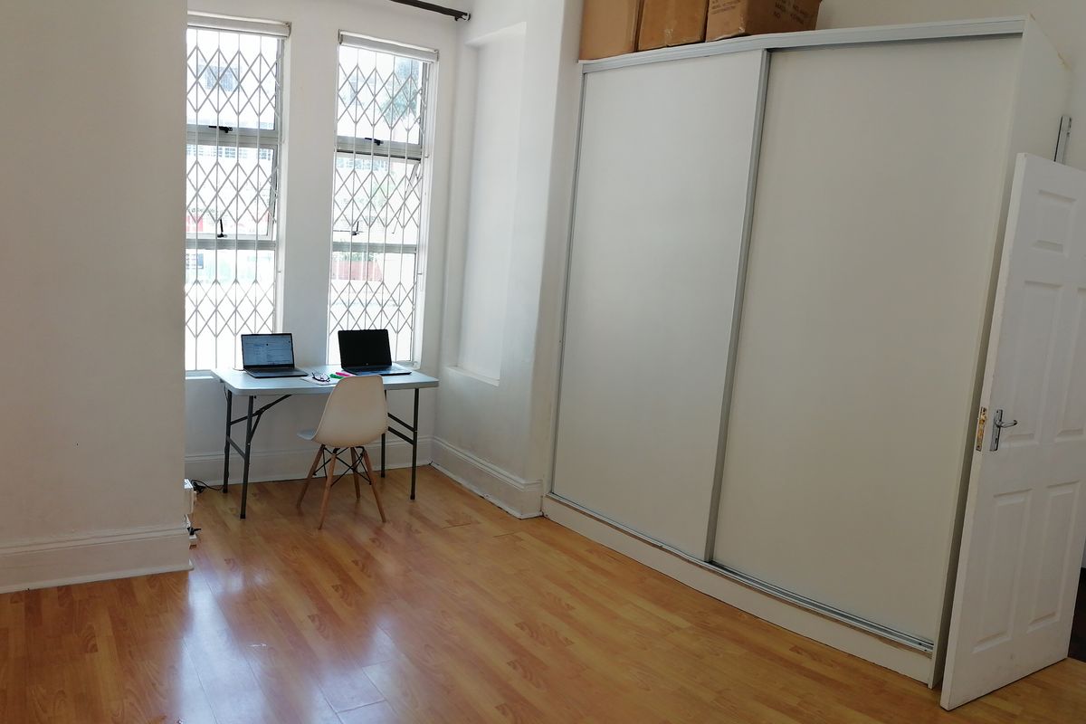 A bright bedroom featuring built-in sliding door wardrobes, laminate wood flooring, and security bars on the windows.