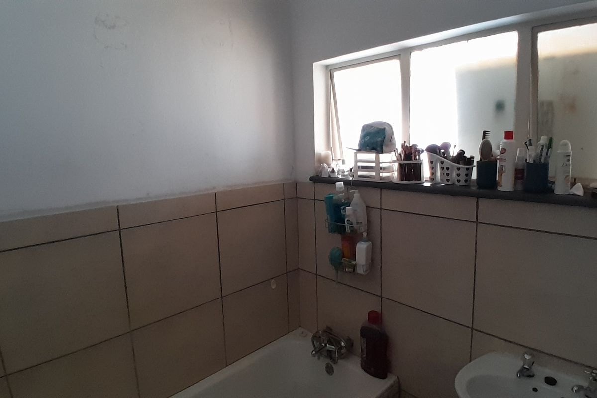 A dated bathroom featuring wall tiles, a standard bathtub, and a basin. The space requires cosmetic updates to improve its overall condition and appeal.
