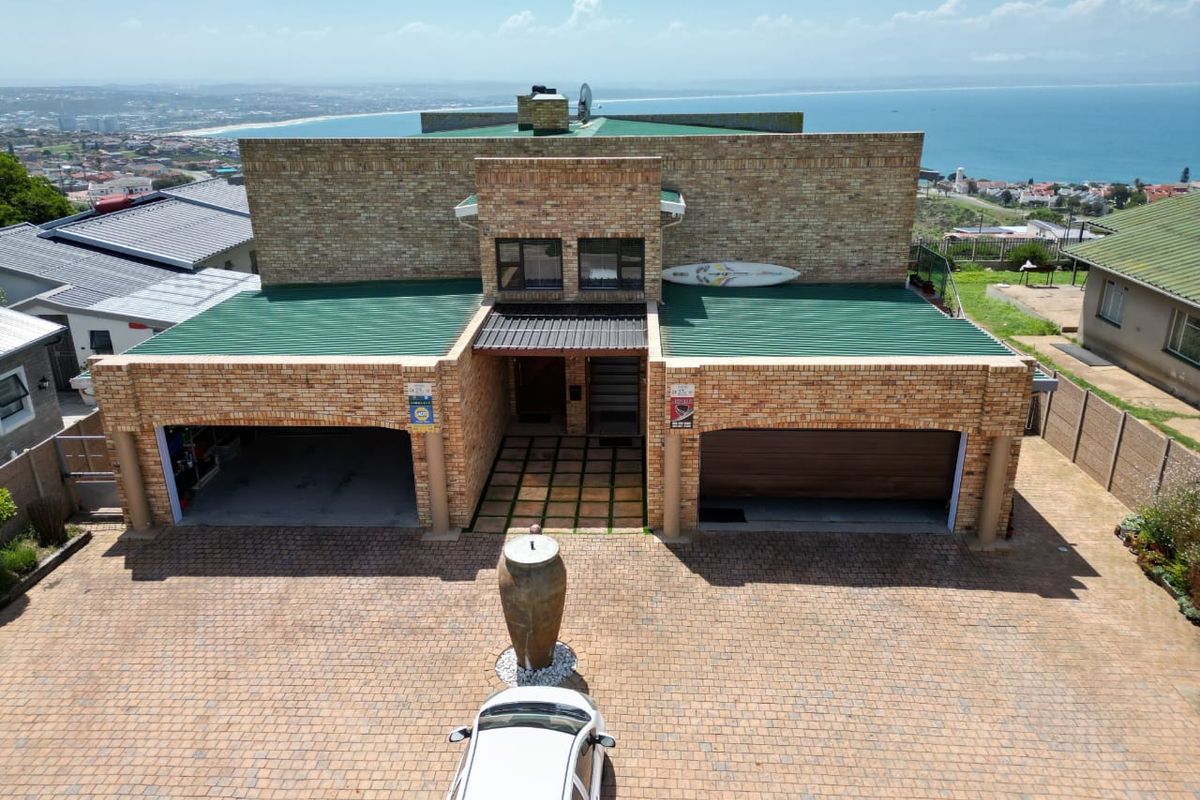 Aerial view of a double-story brick house featuring a paved driveway, double garage, and green metal roofing with coastal views in the background.