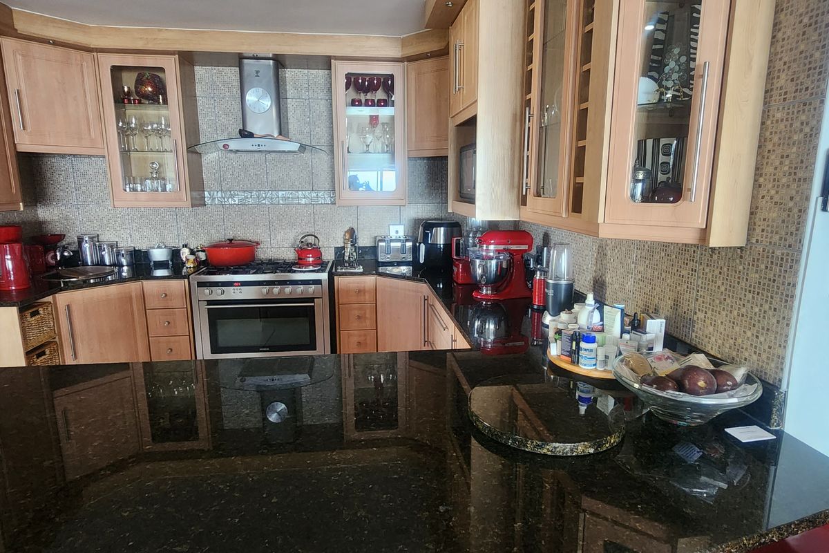A functional kitchen featuring light wood cabinetry, dark granite countertops, a stainless steel gas stove with extractor fan, and mosaic tile backsplash.