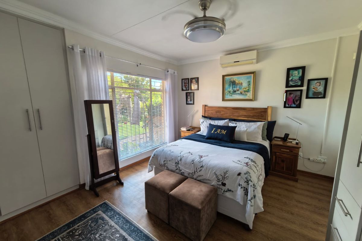 A well-maintained bedroom featuring laminate flooring, built-in cupboards, a ceiling fan, and a split-system air conditioner for climate control.