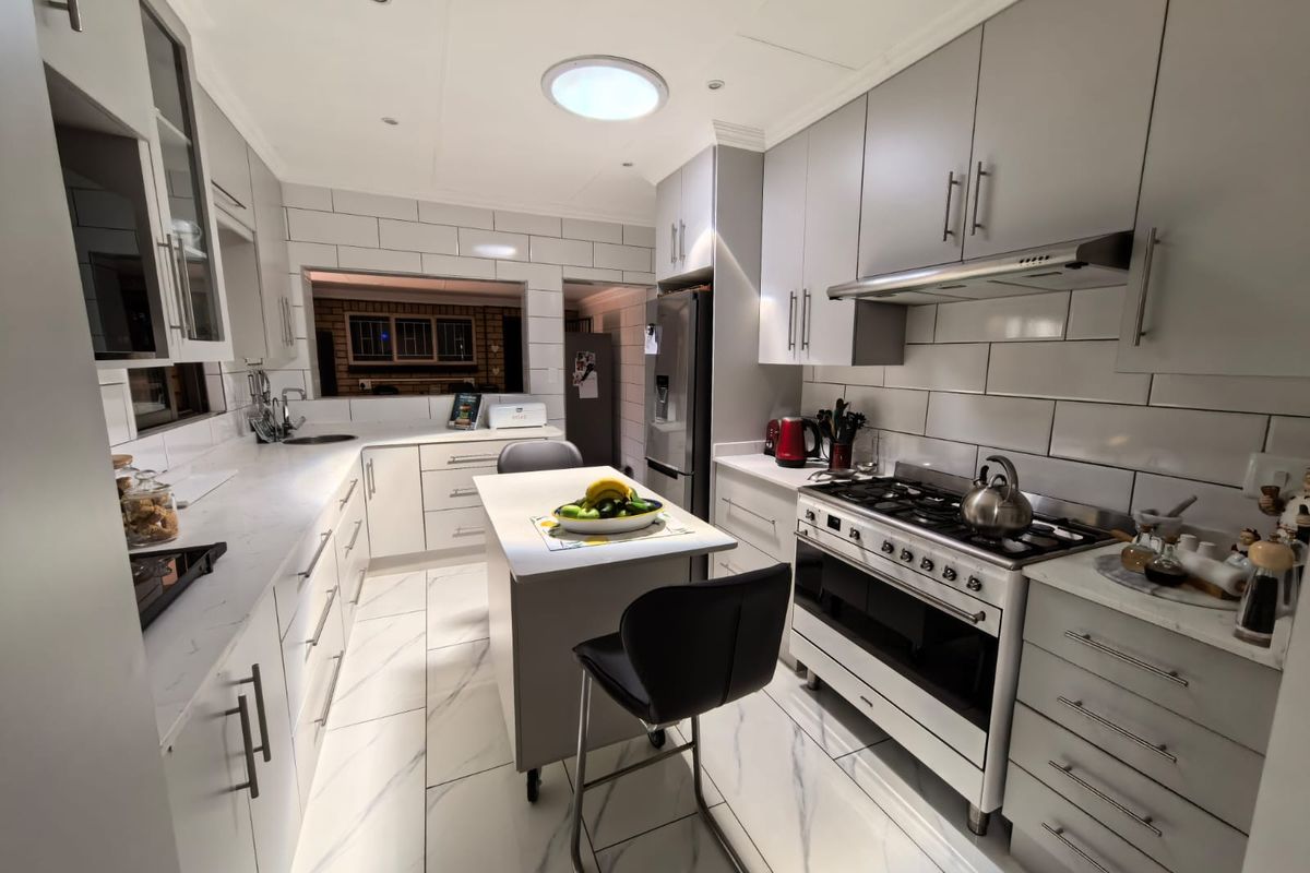 Modern, well-appointed kitchen featuring sleek grey cabinetry, stone countertops, subway tile backsplash, and a central island with marble-look tiled flooring.