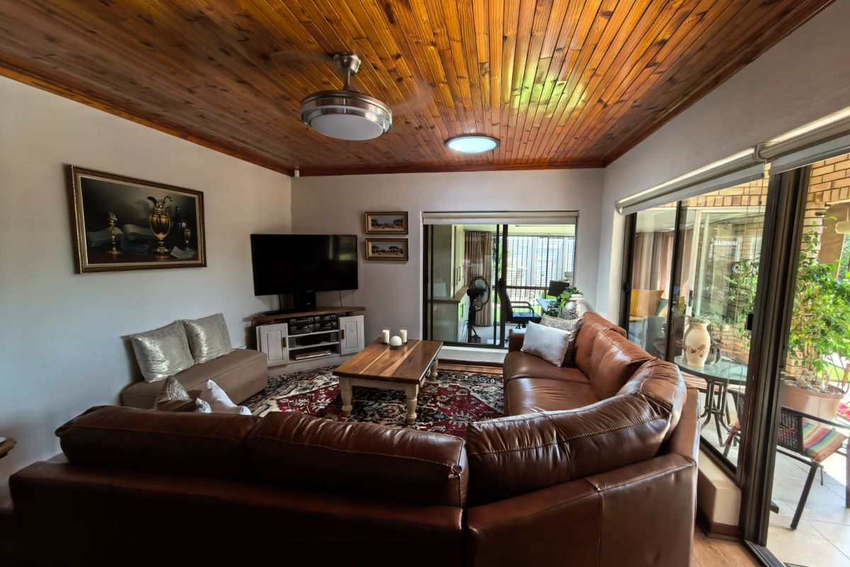 Spacious living room featuring a warm timber tongue and groove ceiling, ceiling fan, and large sliding glass doors providing access to the patio area.