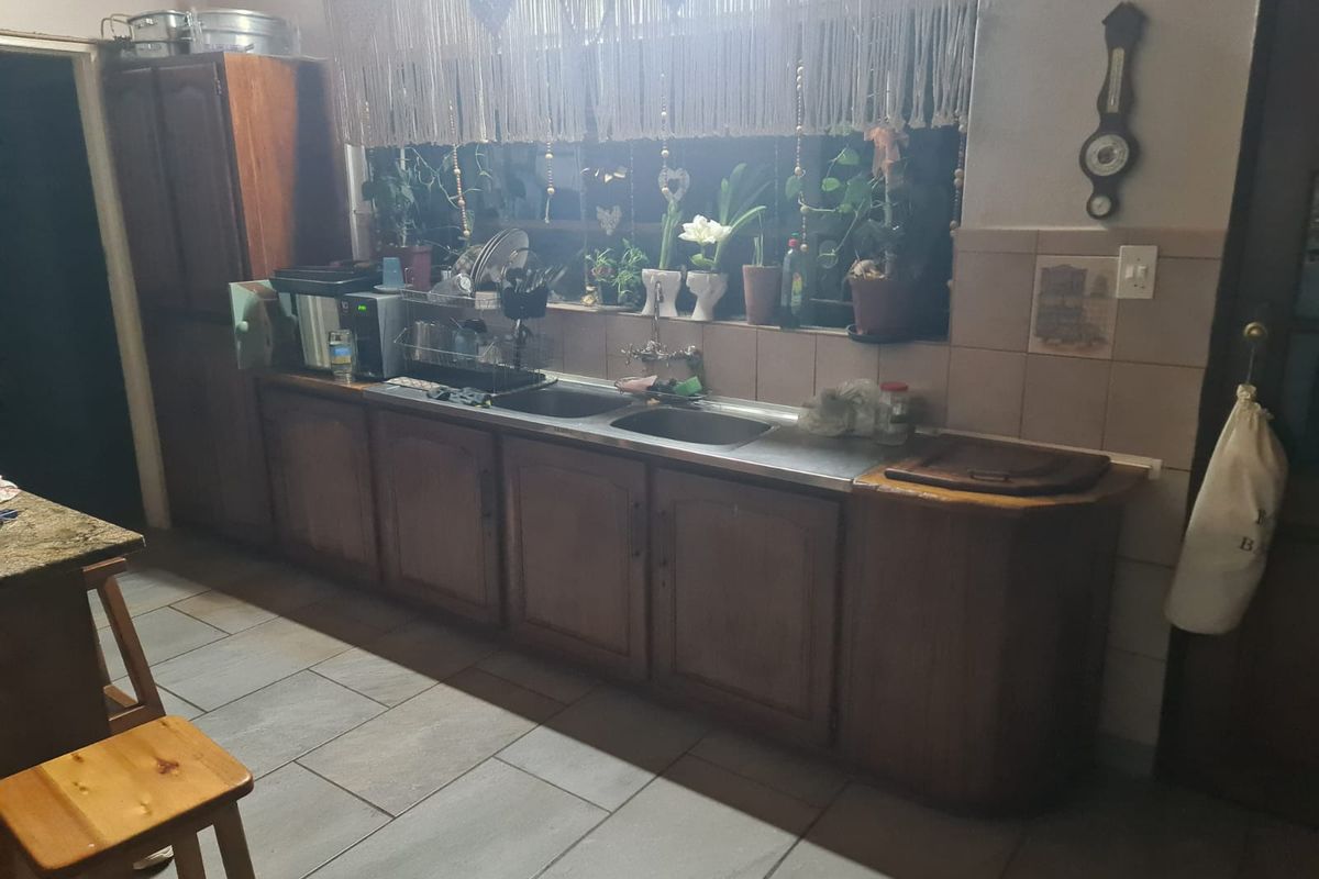 A functional kitchen featuring wooden cabinetry, a double sink with tiled backsplash, and tiled flooring.